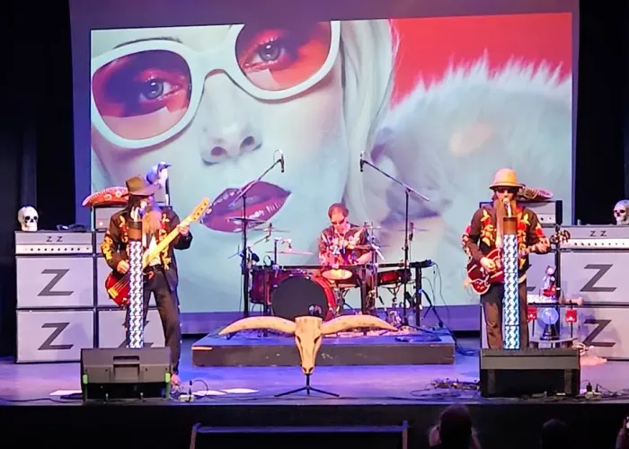 Three band members playing on stage in front of screen